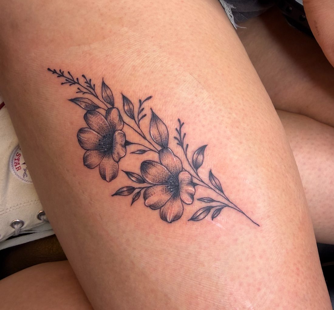 Black and grey floral spray tattoo on the thigh